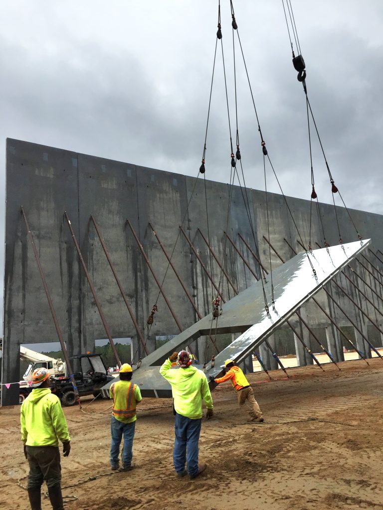 An erecting crew maneuvers a precast concrete wall panel being suspended from a crane.